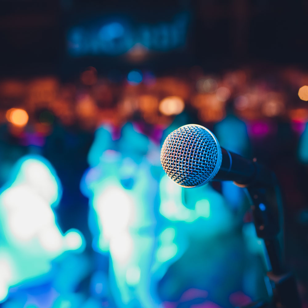 Voorstellingsbeeld van Comedy Night; een microfoon op een onscherpe achtergrond met publiek tijdens een live concert.