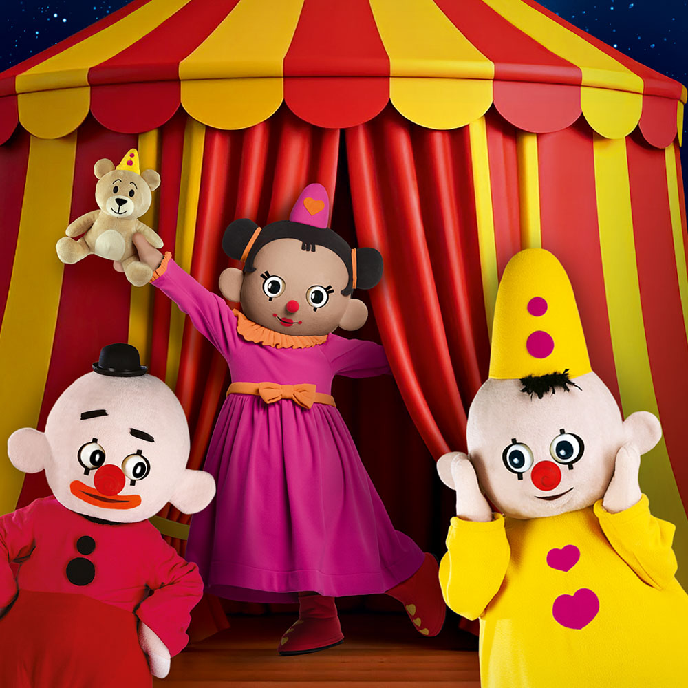 Bumba, Bumbalu en Bumbina poseren vrolijk voor een rood-gele circustent.