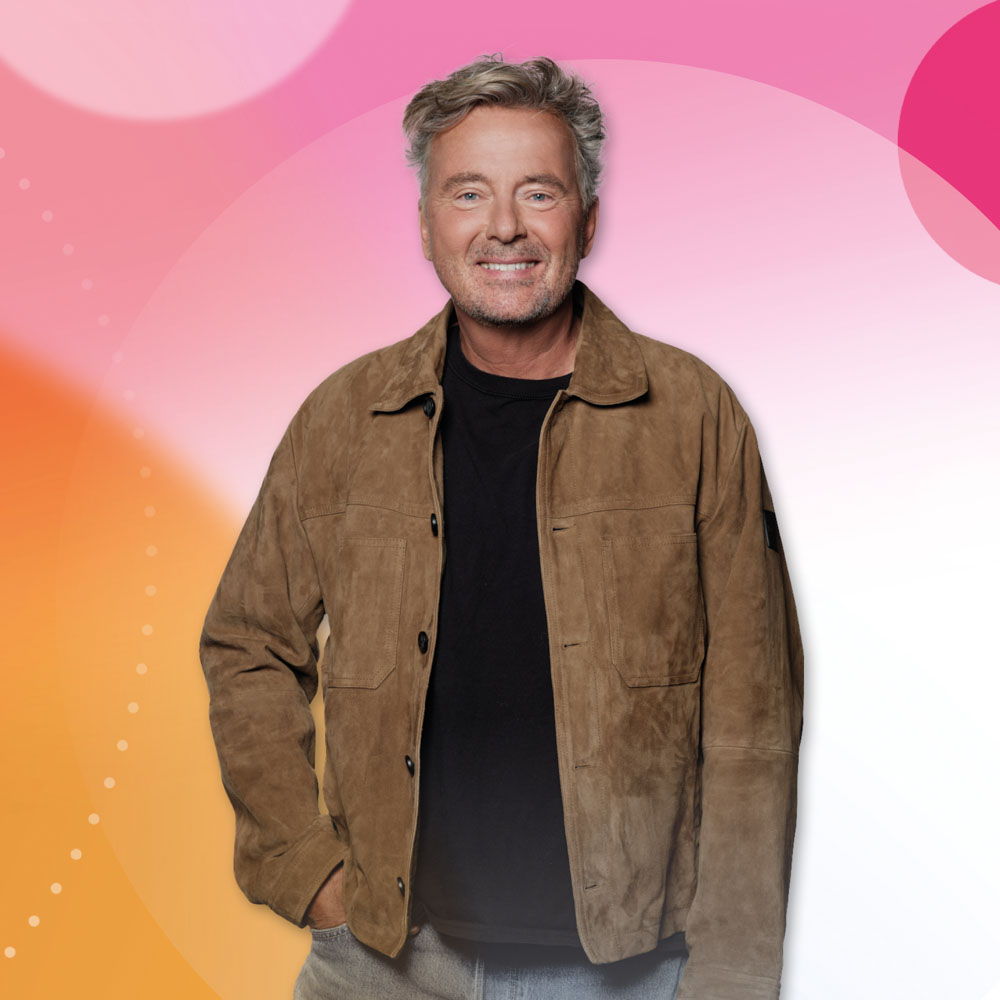 Bert van Leeuwen lacht vriendelijk voor een kleurrijke achtergrond in roze en oranje tinten.