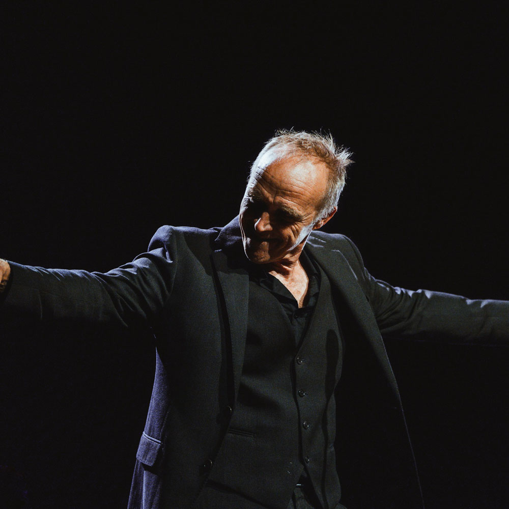 Stef Bos buigt op het podium met gespreide armen in het donker.