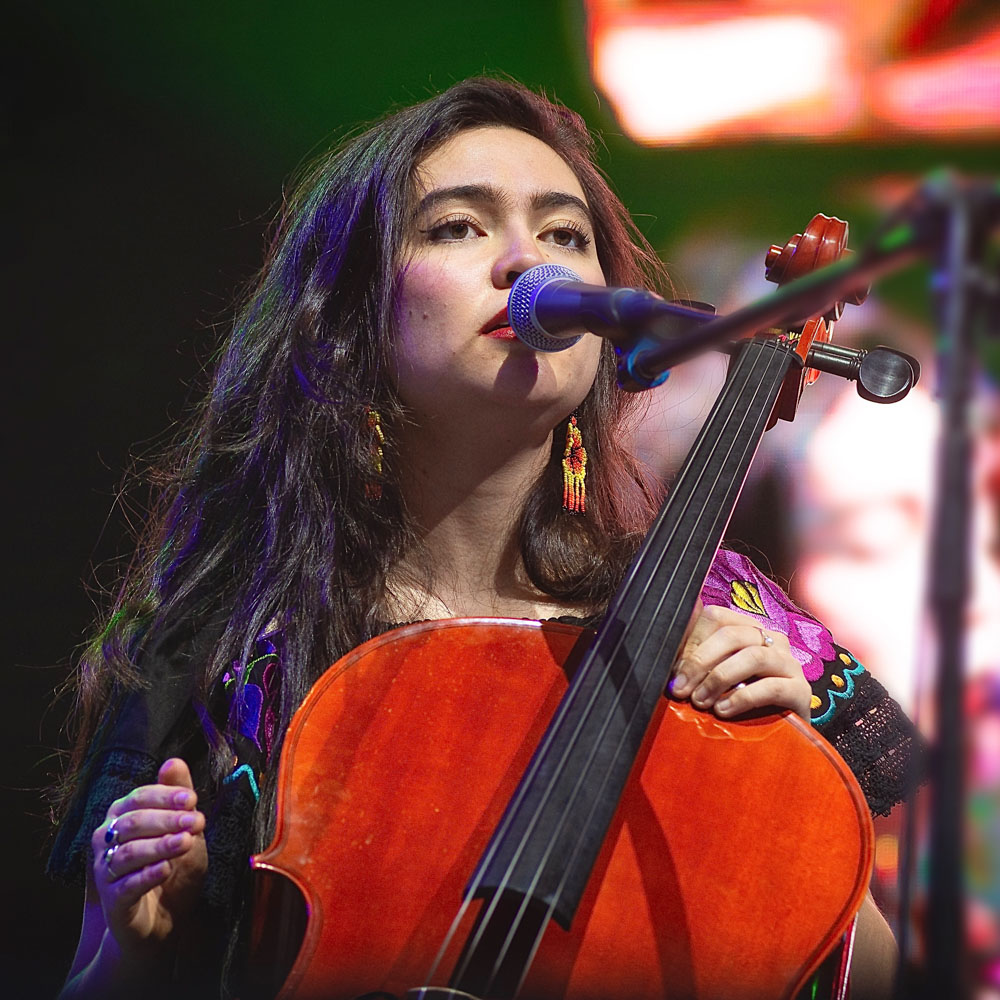 Zangeres Chieko Collective speelt cello en zingt in microfoon op het podium.