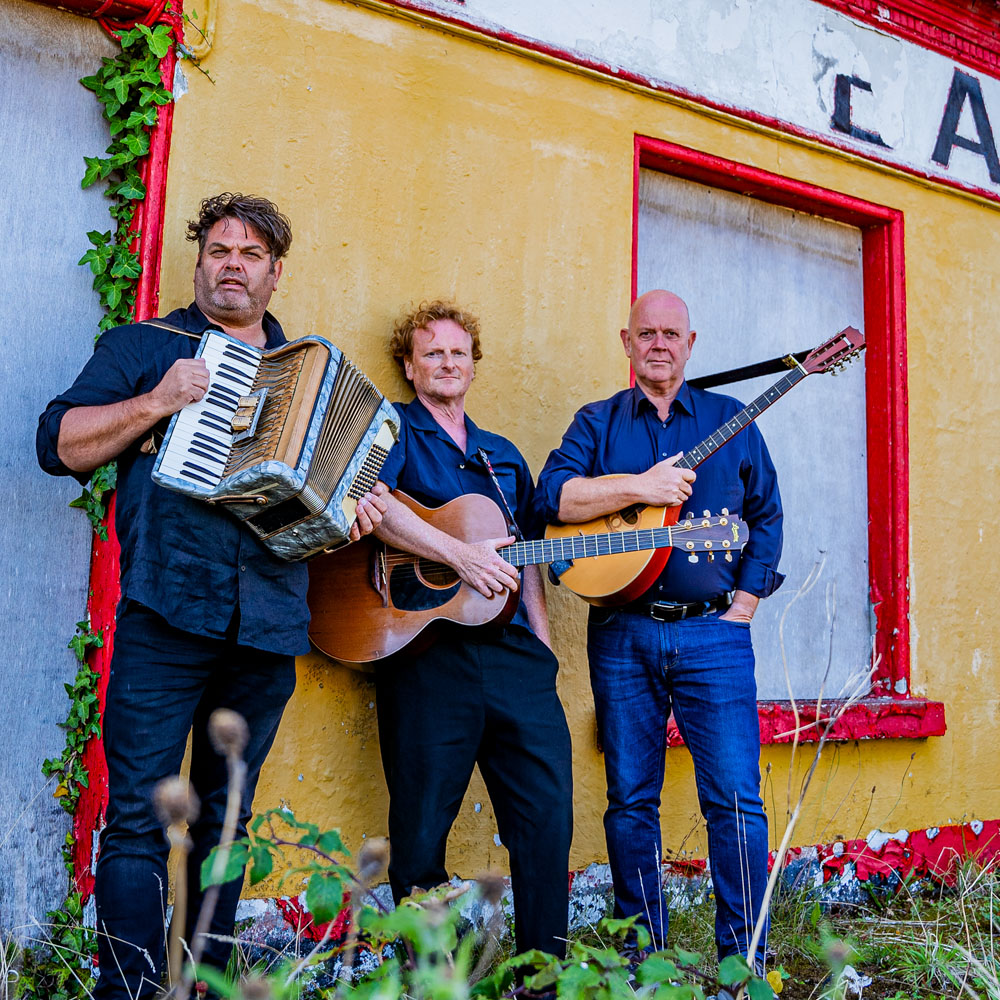 O’dreams poseert met accordeon, gitaar en mandoline voor een verweerde muur.