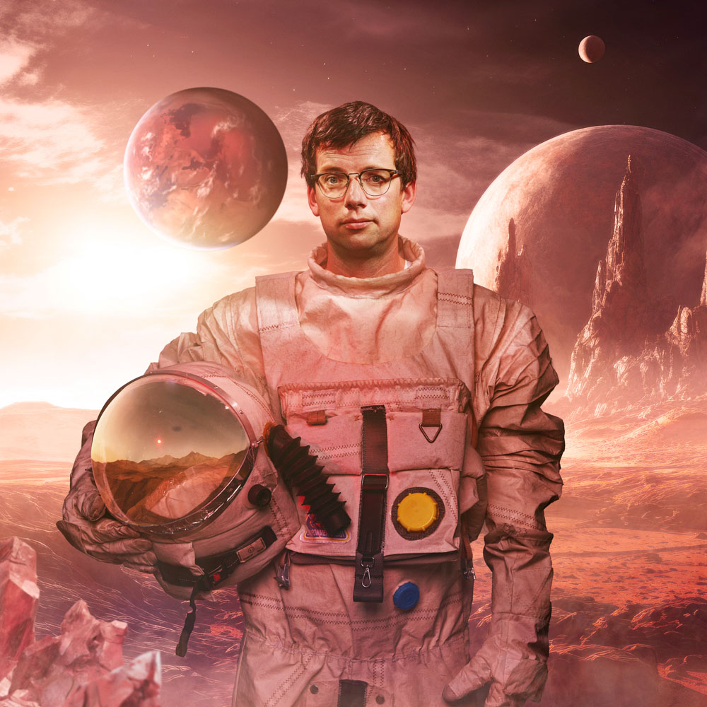 Pieter Derks in ruimtepak met helm in hand op buitenaardse planeet.