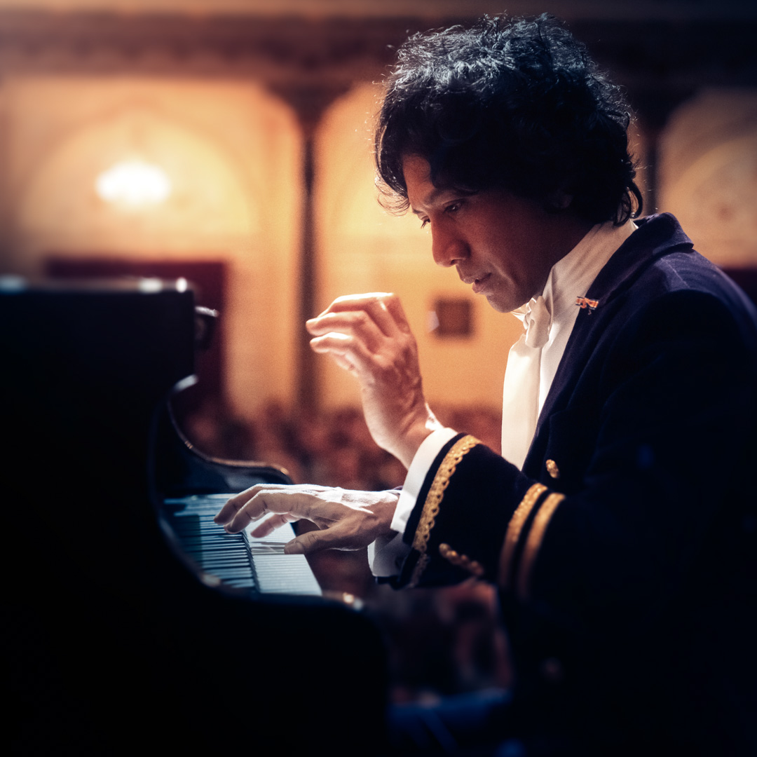 Wibi Soerjadi speelt geconcentreerd vleugel in concertzaal met warm licht.