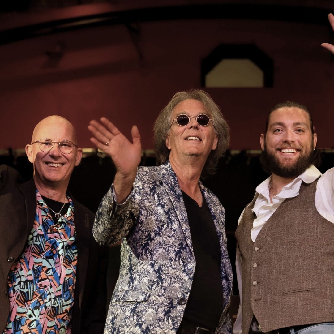 Drie mannen van De Régâhs lachen en zwaaien op het toneel.